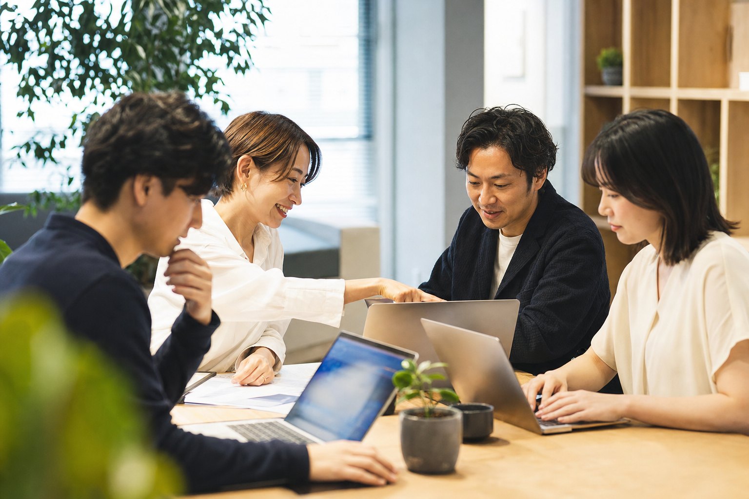 机を囲んだ4人のチームが、ノートPCの画面を見ながら話している